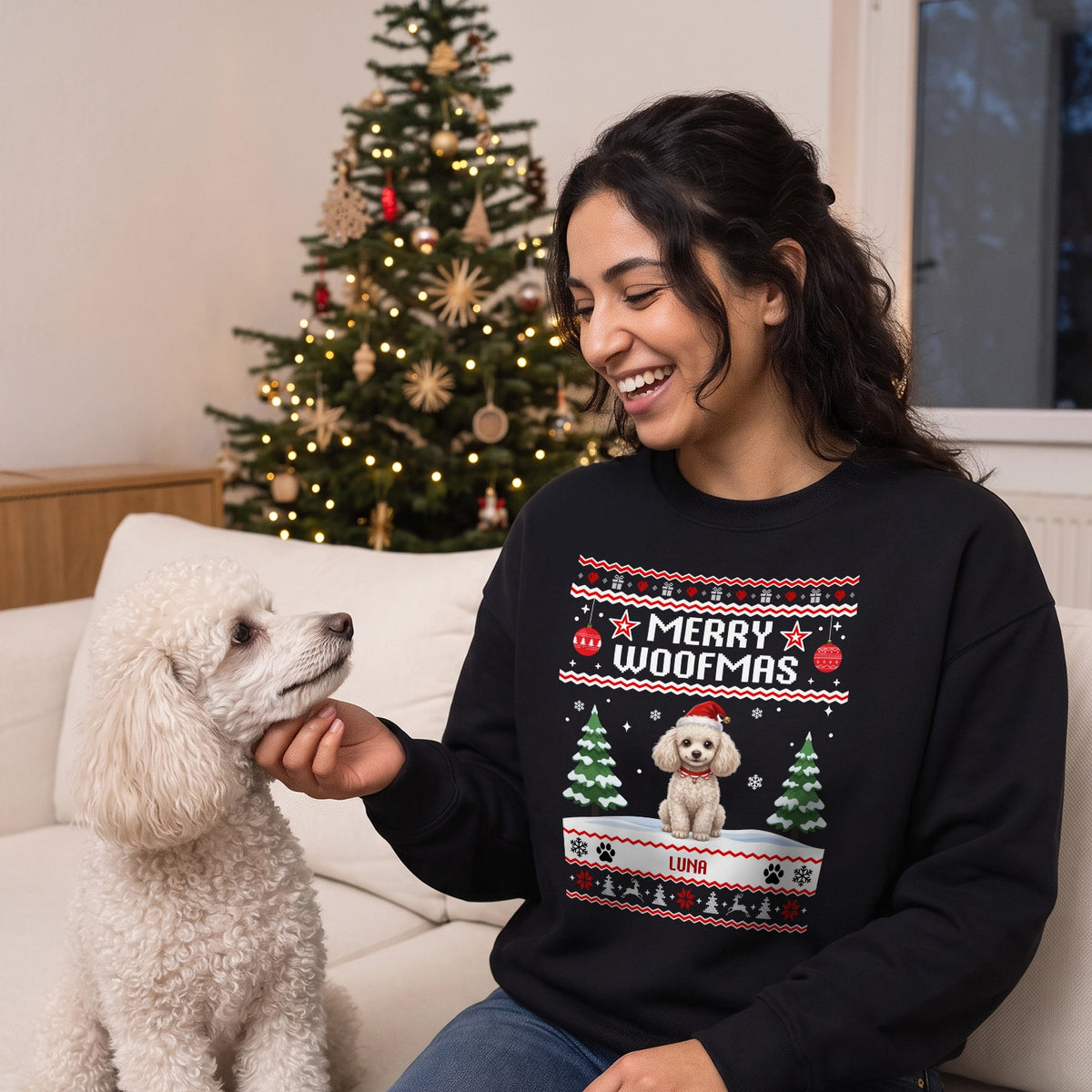 Frau im schwarzen Merry-Woofmas-Pullover mit ihrem weißen Pudel vor dem Weihnachtsbaum