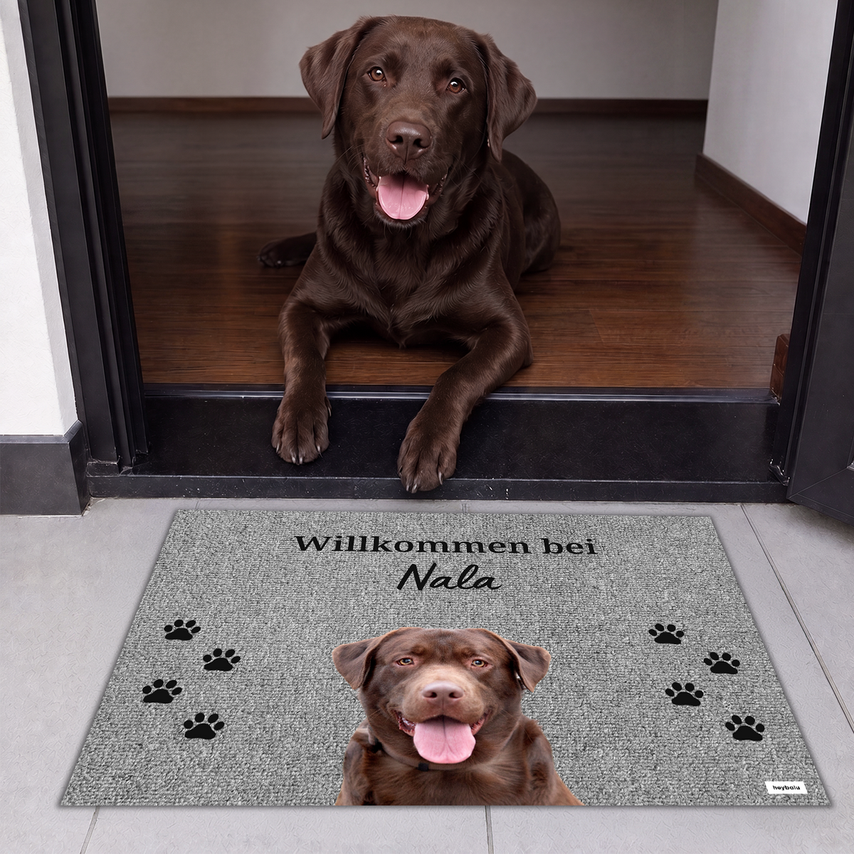Brauner Labrador liegt im Eingang hinter der Fußmatte Willkommen bei Nala mit Pfotenabdrücken
