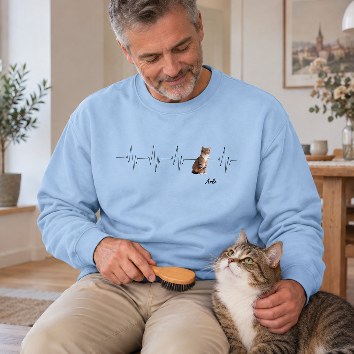 Mann bürstet getigerte Katze im hellblauen Herzschlag-Katzenfoto-Sweater mit Namen