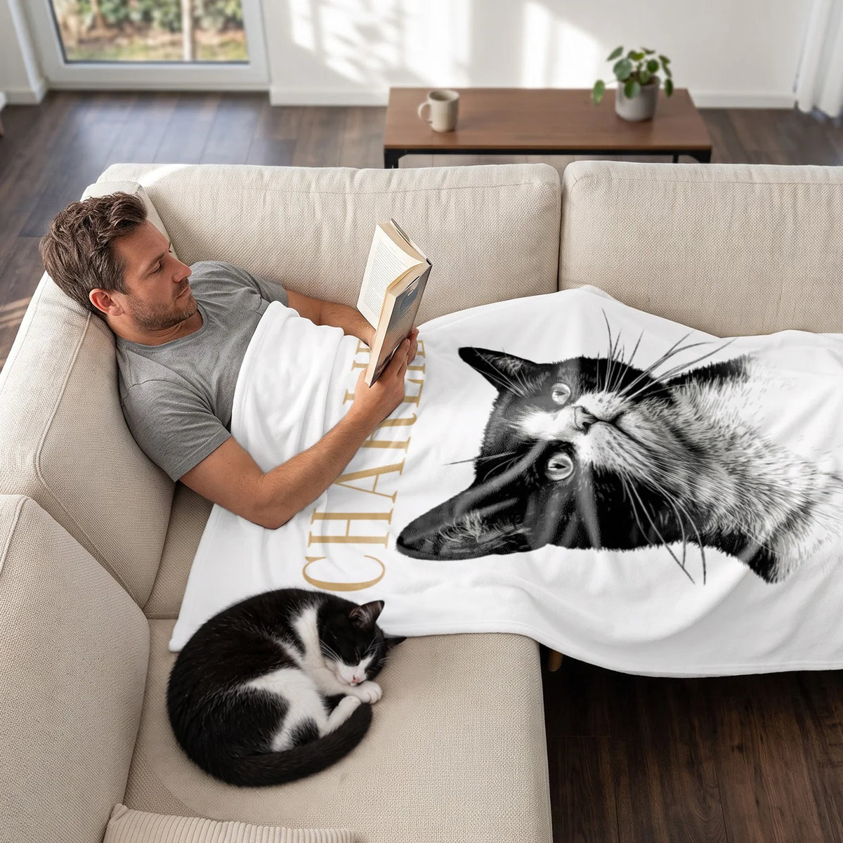 Mann liest auf dem Sofa unter der Retro-Katze-Decke, Katze schläft daneben